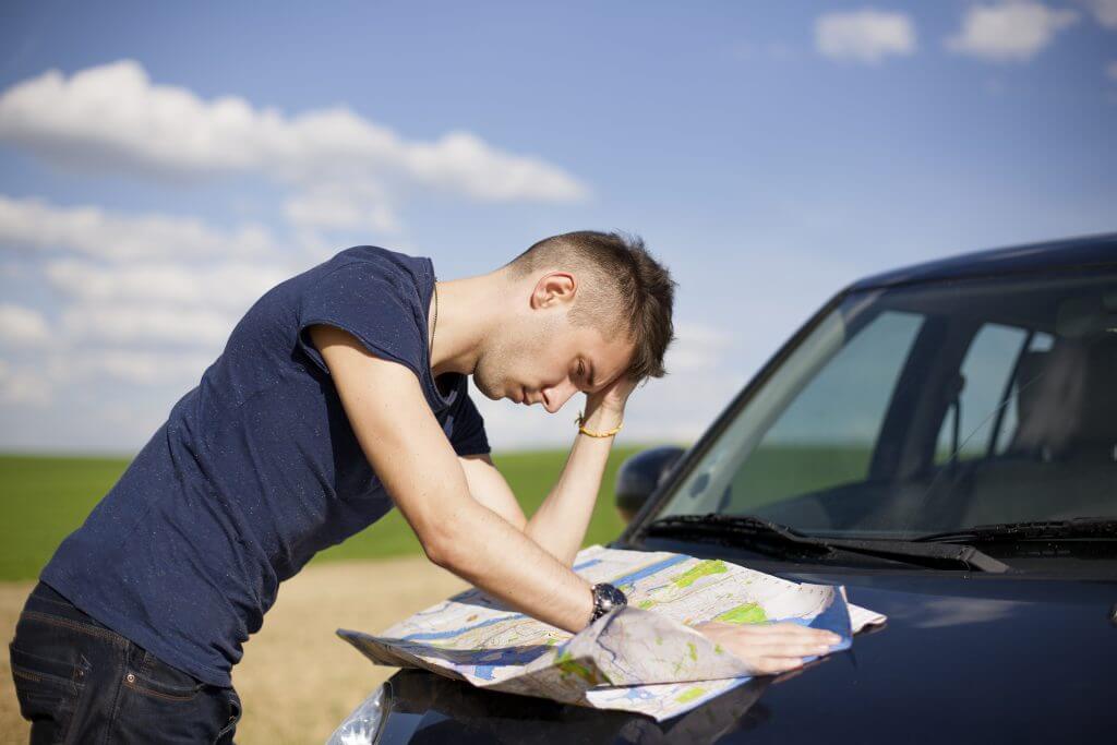 Young man confused looking at a road map outside of his car